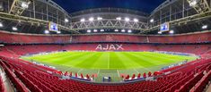 an empty stadium filled with lots of red chairs next to a soccer field at night