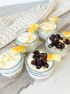 four desserts with lemon slices and blueberries in small glass jars on a counter