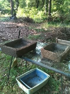 two stone troughs sitting on top of a glass table in the grass next to trees