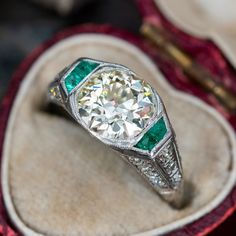 an antique diamond and emerald ring sits in a velvet case on top of a table