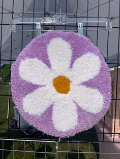 a purple and white flower rug hanging on a wire fence in front of a tent