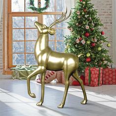 a gold deer statue stands in front of a christmas tree with presents on the floor