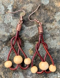 two pairs of brown and white beads are hanging from red leather earwires on a rock