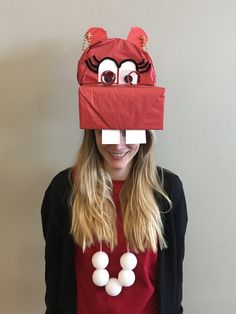 a woman wearing a red bag over her head with eyes and nose painted on it