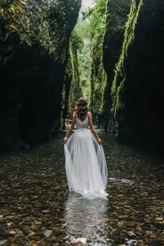 a woman in a white dress is walking through the water with her back to the camera