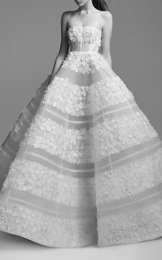 a woman in a white dress with flowers on the skirt and headband, standing against a gray background