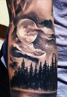 a man's arm with a forest and moon tattoo on it