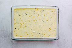 a glass dish filled with yellow sauce on top of a white countertop next to a spoon