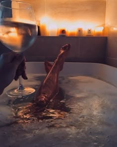 a person holding a wine glass in a bathtub filled with water and brown stuff