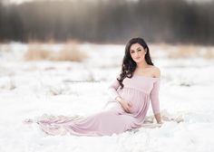 a pregnant woman sitting in the snow wearing a pink dress and posing for a photo