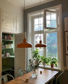 a kitchen table with two hanging lights above it and plants in the window sill