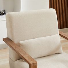 a beige chair with a wooden armrest and seat cushion on the floor in front of a white wall