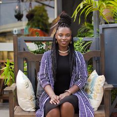 a woman sitting on a wooden bench in front of plants and potted plants,