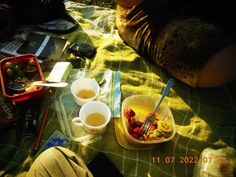 two cups of tea and some fruit on a blanket