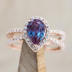 a pear shaped blue and white diamond ring on top of a piece of wood with diamonds around it