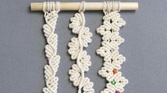 three white crocheted necklaces hanging from a wooden hanger on a gray surface