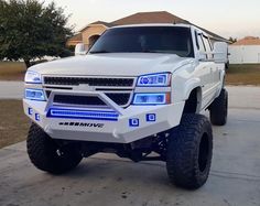 a white truck parked in front of a house with blue lights on it's hood