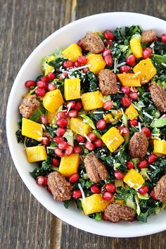 a white bowl filled with meat, vegetables and pomegranates on top of a wooden table