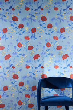 a blue chair sitting in front of a wall with red and yellow flowers on it