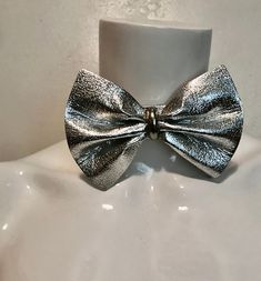 "1980's silver vinyl bow tie. Try it instead of a necklace...or all on its own Good size bow; 3 1/4\"h x 4 3/4\"w with metal center piece. Silver metal hook and chain at back allows for adjustments. No maker. Very good condition. total length 15\" strap 1\"w x 10 7/8\"l chain 3 1/2\"" Adjustable Bow Tie Jewelry For Party, Adjustable Party Jewelry With Decorative Bow, Adjustable Bow Jewelry For Evening, Silver Bow Jewelry For Evening, Silver Bow Jewelry For Party, Silver Butterfly Knot Jewelry For Party, Silver Jewelry With Butterfly Knot For Party, Silver Party Jewelry With Satin Bow, Silver Jewelry With Satin Bow For Party