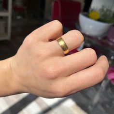 a person's hand with a gold ring on their left thumb and a plant in the background