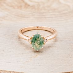 a ring with a green and white stone in the center on top of a piece of wood