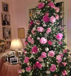 a decorated christmas tree with pink flowers and ornaments on it in a living room area