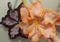 two crocheted flowers are being held up by someone's hand on the wall