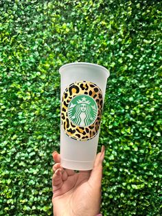 a hand holding up a starbucks cup in front of a green wall with leaves on it