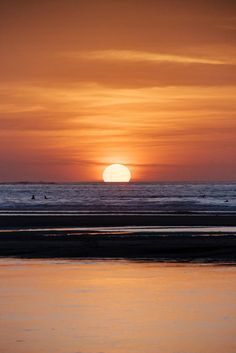 the sun is setting over the ocean with surfers