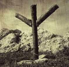 a wooden cross sitting on top of a grass covered field next to rocks and trees