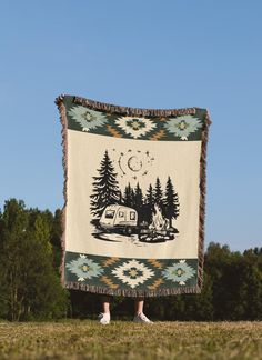 a person standing in front of a blanket with a camper and trees on it