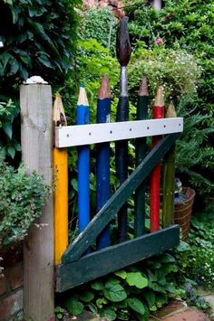 a fence made out of colored pencils in front of some bushes and trees,