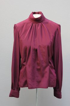 "DESCRIPTION: Long sleeves  Ruched cuffs with 2 button closures Collar is ruched with pleats at the center Pleats at the waist  Small shoulder pads  8 wine colored irridiscent buttons down the back TAG/LABEL:  Anna Kriste, 100% Polyester, Size 10 APPROXIMATE MEASUREMENTS (Measured Flat): Bust 42\" Sleeve Length 24\" Armhole 7\"  Shoulder to Shoulder 16\" Length 23\" CONDITION:  Blouse is in excellent condition!  I found no issues." Purple Long Sleeve Evening Blouse, Classic Fitted Tops With Pleated Sleeves, Fitted Tops With Pleated Sleeves For Fall, Classic Fitted Blouse With Gathered Sleeves, Fall Evening Blouse With Ruched Details, Formal Tops With Pleated Bishop Sleeves, Formal Top With Pleated Bishop Sleeves, Formal Puff Sleeve Tops For Fall, Fall Evening Ruched Blouse