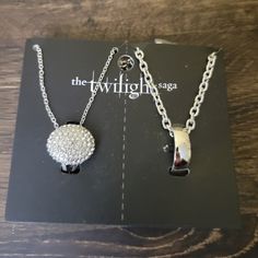 two silver necklaces sitting on top of a black and white card with the twilight saga logo