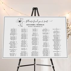 the seating chart for this wedding is displayed on a easel with lights in the background