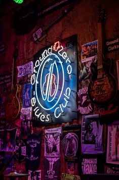 a neon sign on the side of a wall covered in posters and other memorabilias