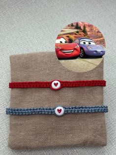 two bracelets with cars on them sitting next to each other in front of a piece of fabric