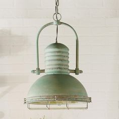 a green light fixture hanging from a brick wall next to a potted plant on a table