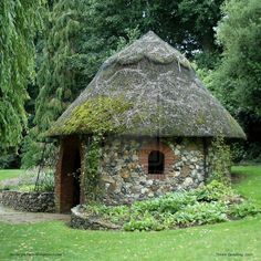 an old stone building with a thatched roof in the middle of a park area