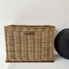 a wicker basket next to a black fan on a white surface with a wall in the background