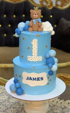 a blue and white cake with a teddy bear sitting on it's top tier