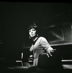 a black and white photo of a woman standing in front of a computer desk with her hands out