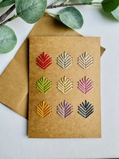 four different colored leaves are placed on top of a brown card next to some green leaves