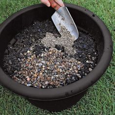 a person scooping gravel into a black pot on the grass with a spatula