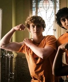 two young men flexing their muscles in front of a stained glass window at home