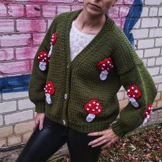 a woman standing in front of a brick wall wearing a green cardigan with red mushrooms on it