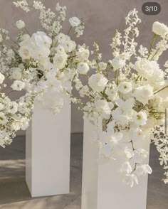 three white vases with flowers in them sitting on a cement floor next to each other