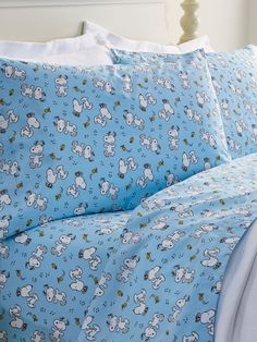 a bed covered in blue and white sheets with cartoon animals on them, next to a night stand