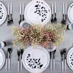 the table is set with white plates and black utensils, silverware, and baby's breath flowers